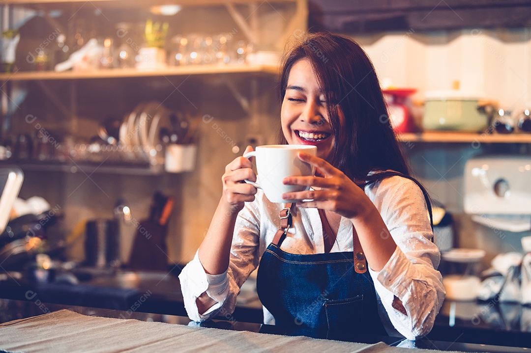 Feliz barista asiática segurando uma xícara de café e provando.