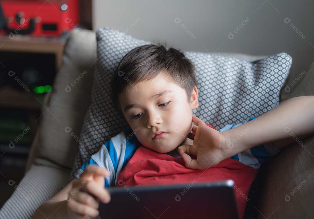 Menino usando tablet jogando jogo na internet, Criança sentada no sofá assistindo ou conversando com um amigo online