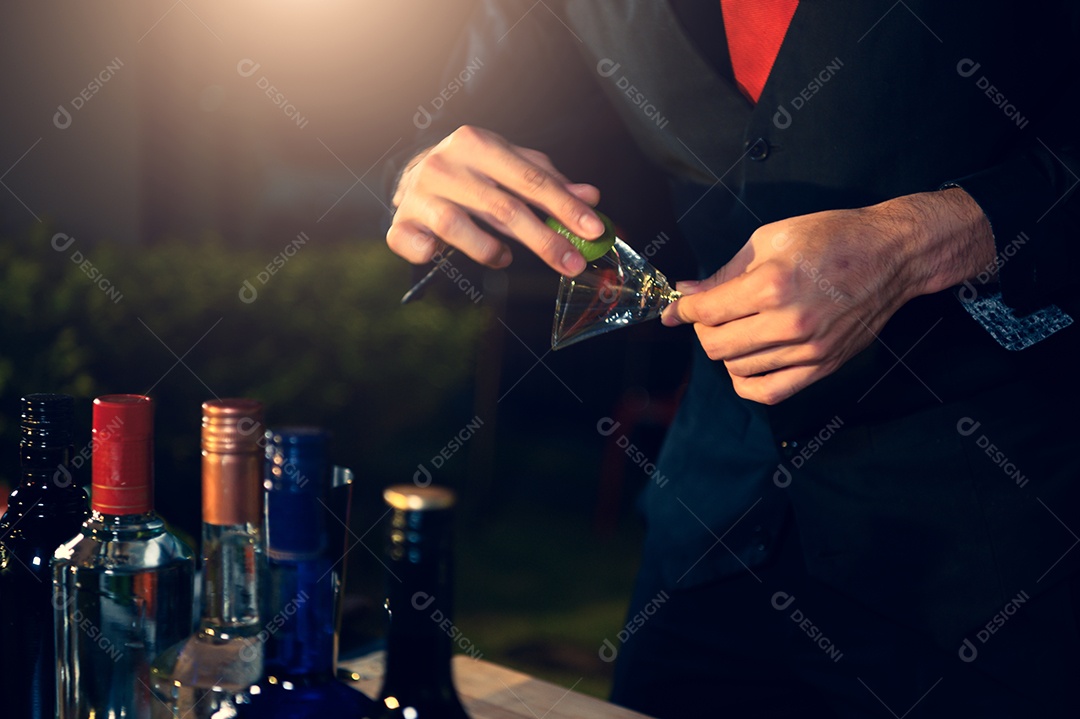 Barman profissional preparando coquetel de limonada de limão fresco em copo de vinho com gelo no bar noturno.