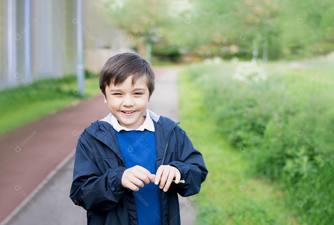 Garoto bonito da escola soprando flor-leão no parque primavera enquanto caminhava para a escola pela manhã.