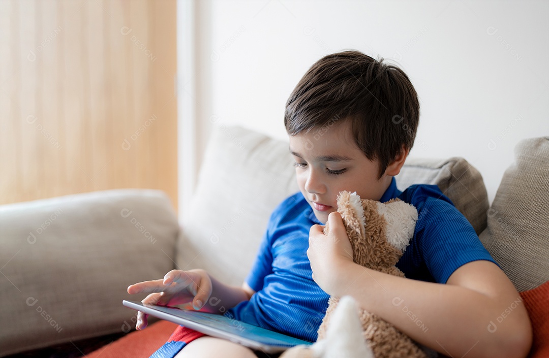 Menino de retrato jogando jogo no tablet sentado no sofá com luz brilhando da janela