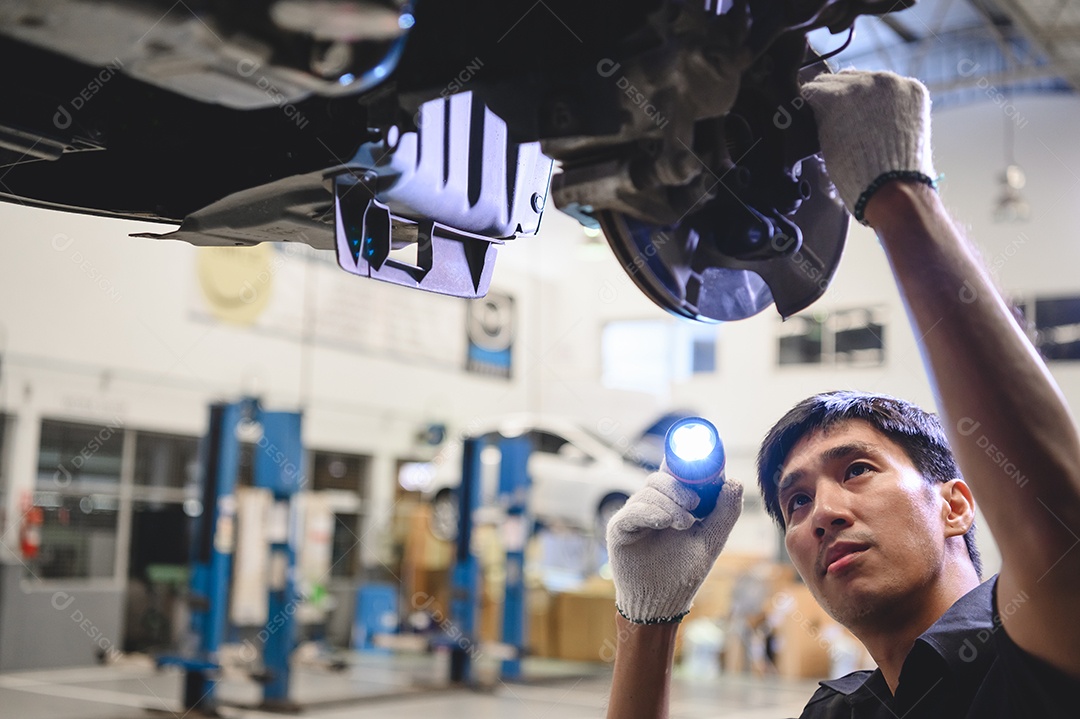 Segure mecânico masculino asiático e lanterna brilhante para examinar o carro.