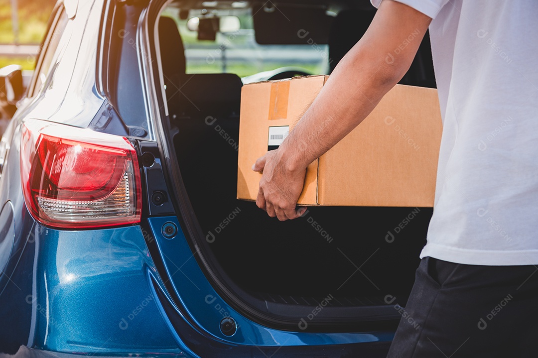 O entregador está entregando caixas de papelão aos clientes pela porta do porta-malas de um carro particular.