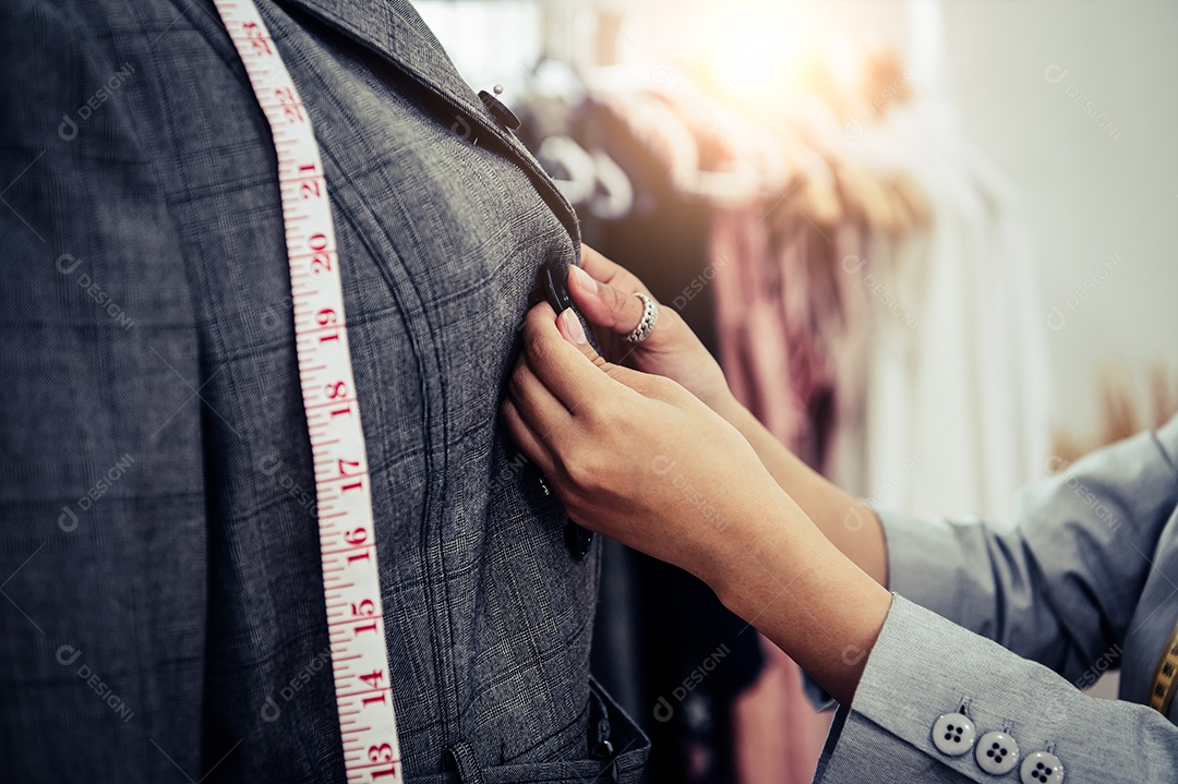 Close-up da mão de menina designer de moda feminina fazendo caber nas roupas uniformes de terno formal no modelo de manequim.