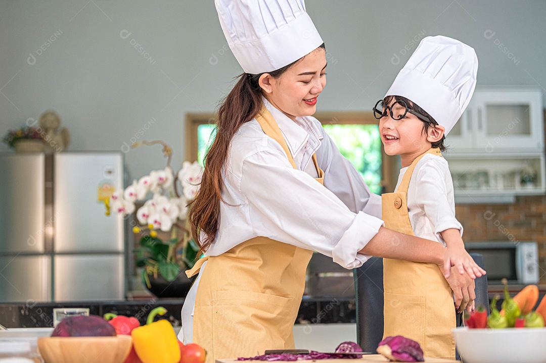 Feliz linda mulher asiática veste roupa de chef de menino bonitinho para se preparar para cozinhar na cozinha de casa.
