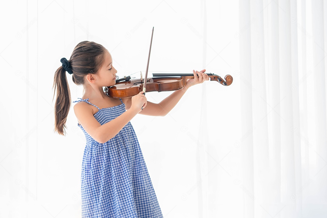 Menina bonitinha tocando violino no quarto com fundo de cortina branca.
