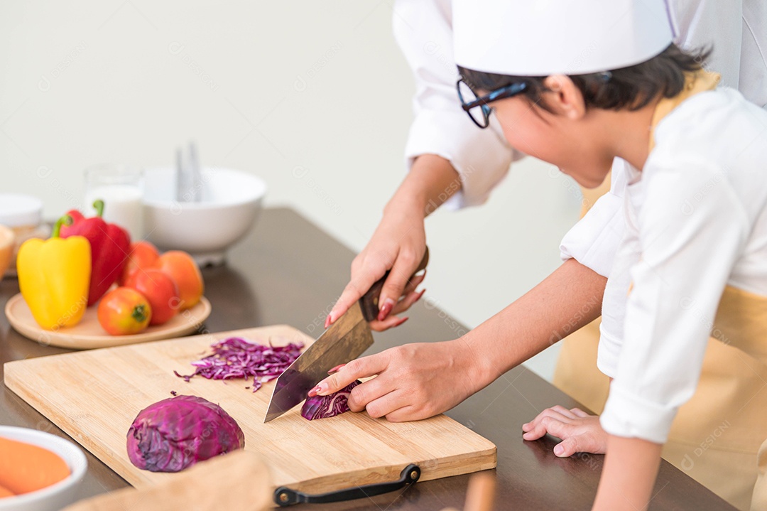 Close-up da mão da mãe que corta o repolho roxo na placa de madeira.