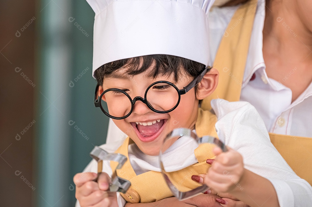 Menino bonito e feliz asiático interessado em cozinhar com a mãe.