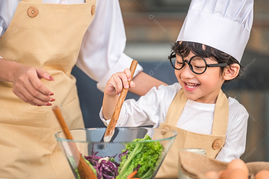 Menino bonito e feliz asiático interessado em cozinhar com a mãe.