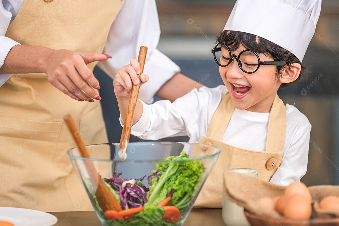 Menino bonito e feliz asiático interessado em cozinhar com a mãe.