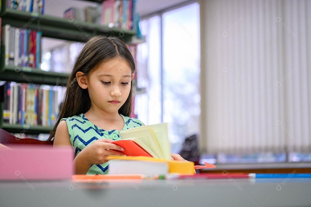 Menina bonitinha lendo livros na biblioteca atentamente na escola.