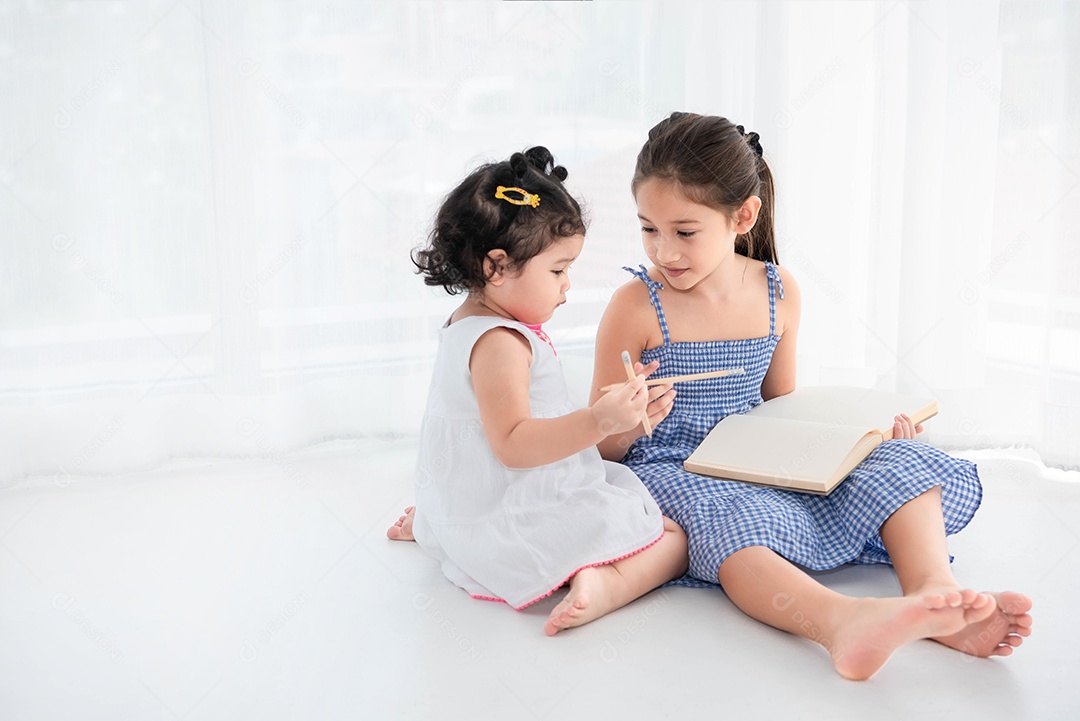 Two happy sisters drawing in sketchbook together at home.