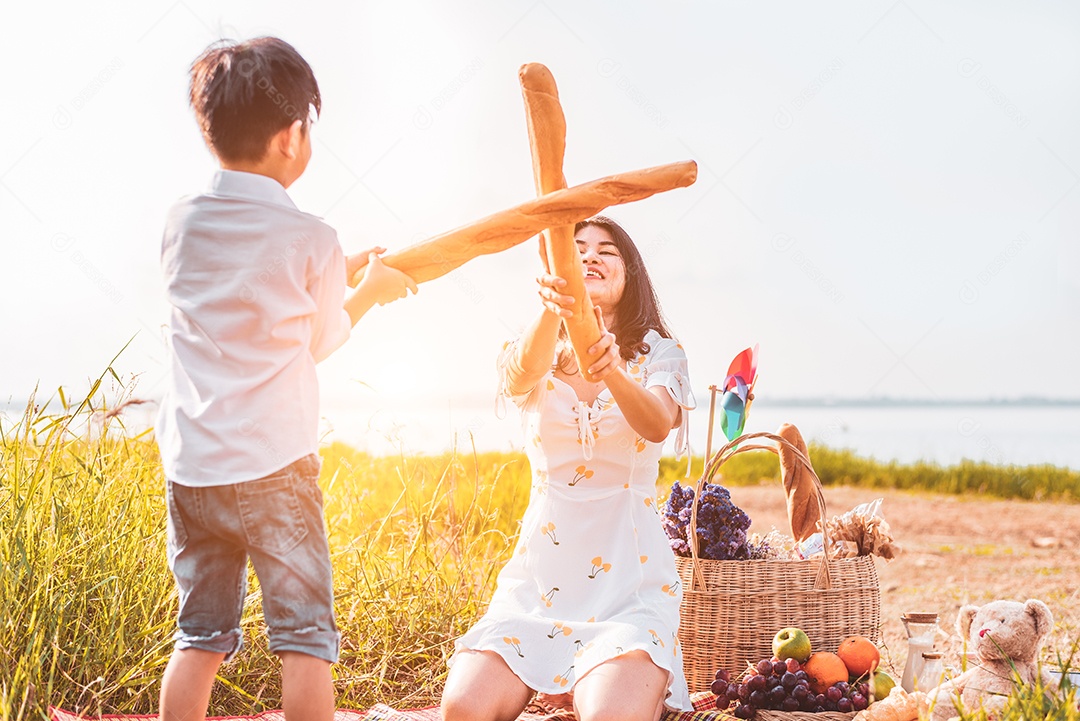 Mãe e filho jogam esgrima com pão juntos quando fazem piquenique.