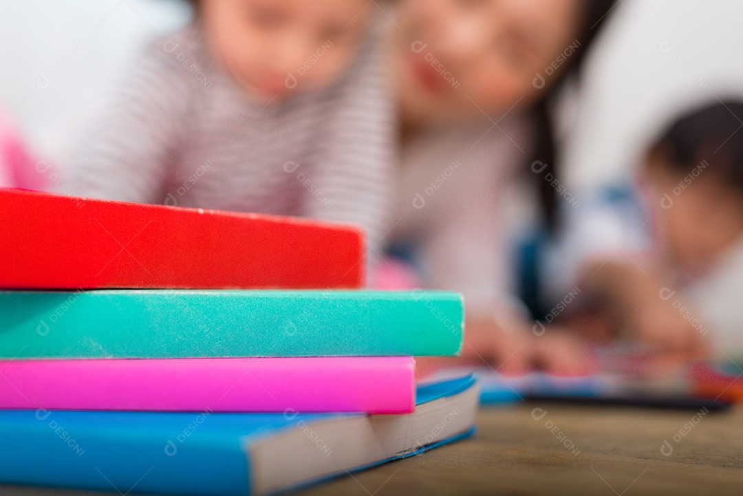 Pilha de livro colorido no chão com mulher embaçada e dois filhos.