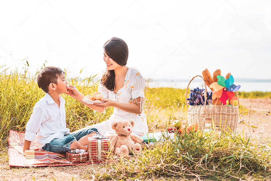 Linda mãe asiática alimentando lanche para seu filho no prado.