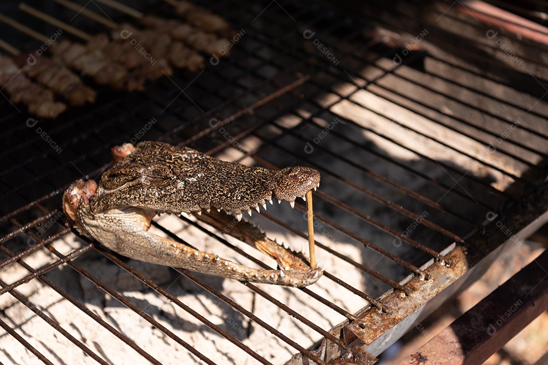 Close-up da cabeça de crocodilo assado no fogão a carvão no mercado de rua. Comida e conceito de cozinha exótica.