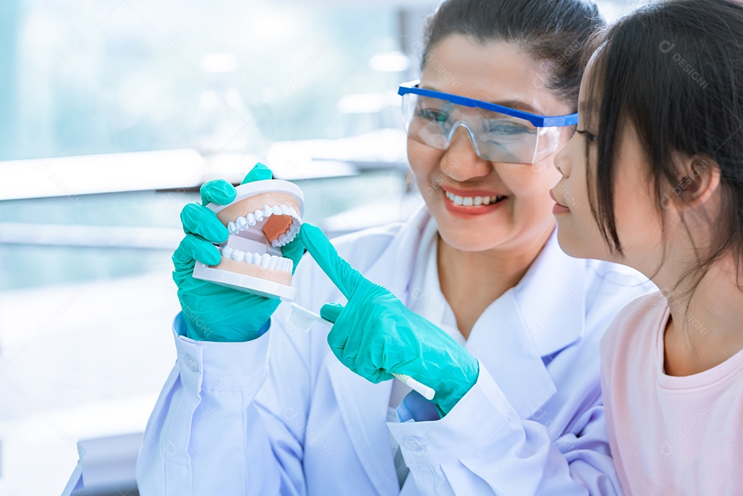 Menina aprendendo a escovar os dentes com dentista feminina.