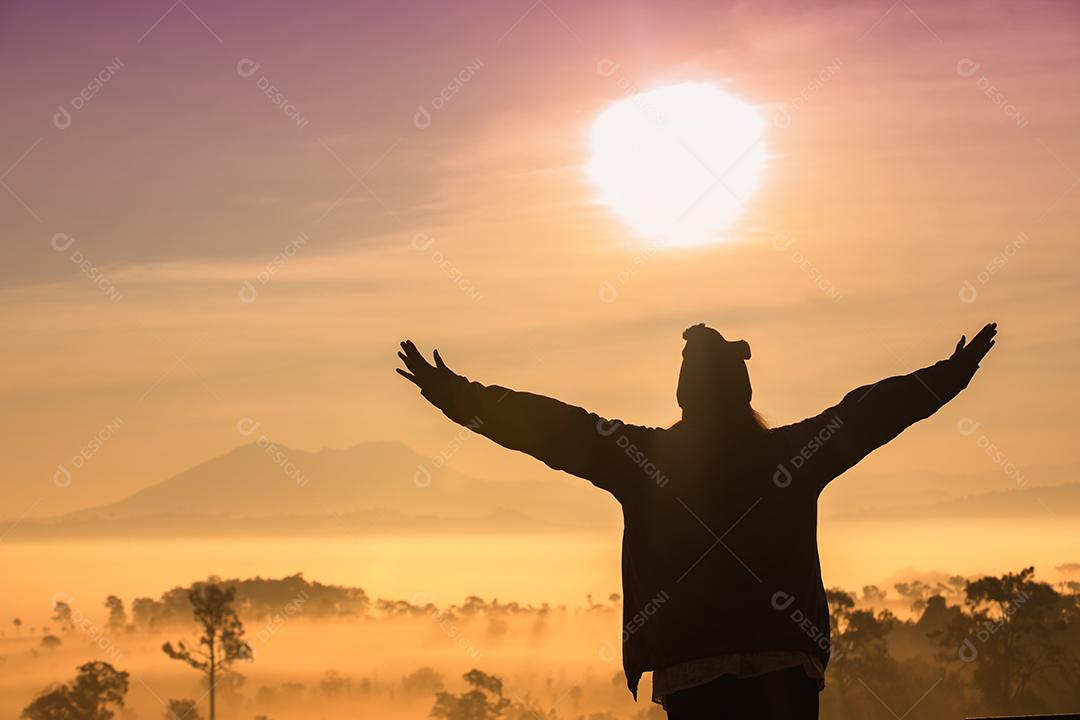 Silhueta de mulheres viajantes da liberdade de pé com os braços levantados e desfrutando de uma bela natureza e torcendo jovens ao pôr do sol e nevoeiro