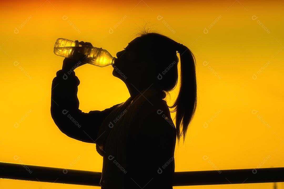 Imagem de silhuetas de mulher asiática desportiva bebendo água ao ar livre e foco suave