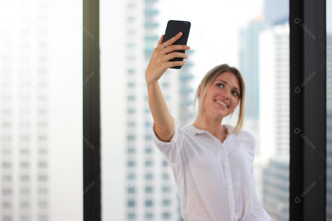 Retrato de uma jovem atraente fazendo foto selfie em smartphone no fundo de um prédio de escritórios moderno