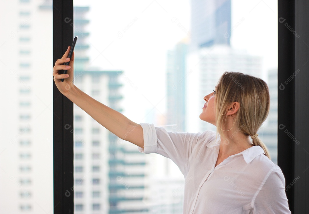 Retrato de uma jovem atraente fazendo foto selfie em smartphone no fundo de um prédio de escritórios moderno