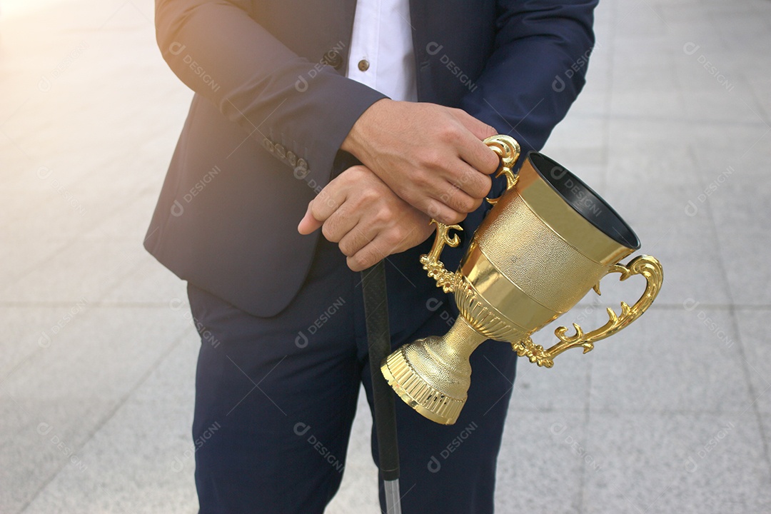 Homem de negócios de sucesso em terno segurando o prêmio da taça de ouro