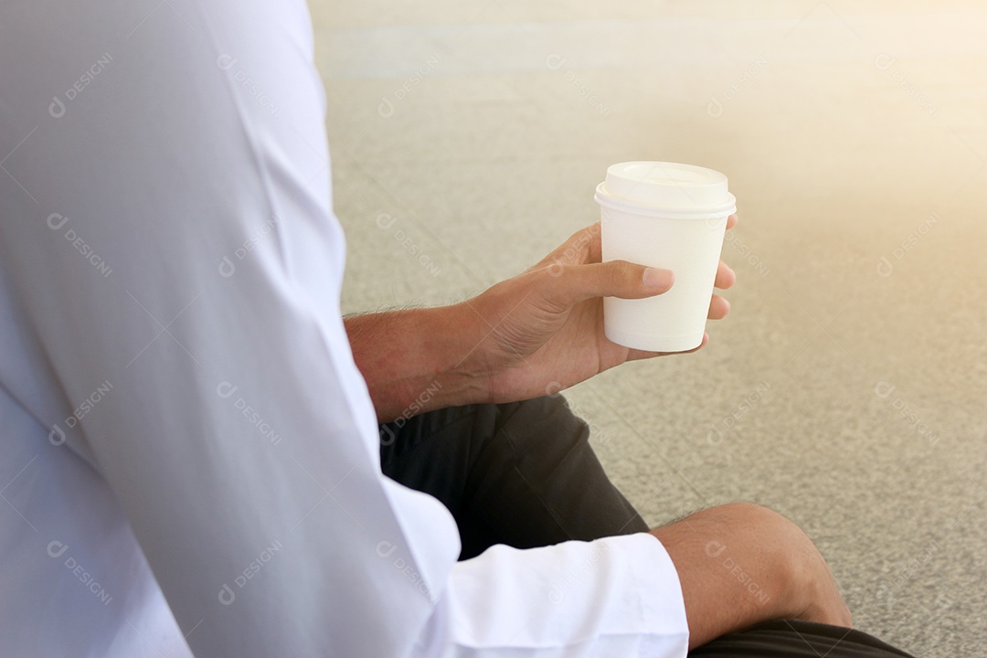 Jovem sentado bebendo café de copo descartável e smartphone