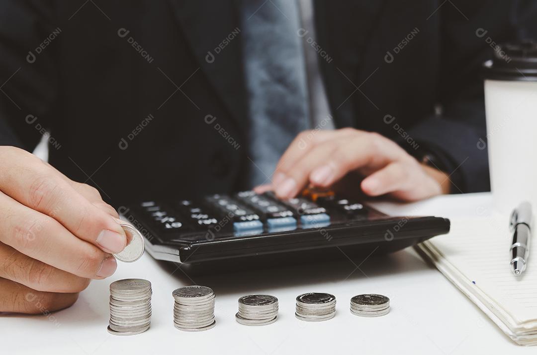 Mão de pessoa de empresário segurando o dinheiro da pilha de moedas e calculadora na mesa conceito de seguro de contabilidade de investimento de finanças de negócios crescimento fiscal