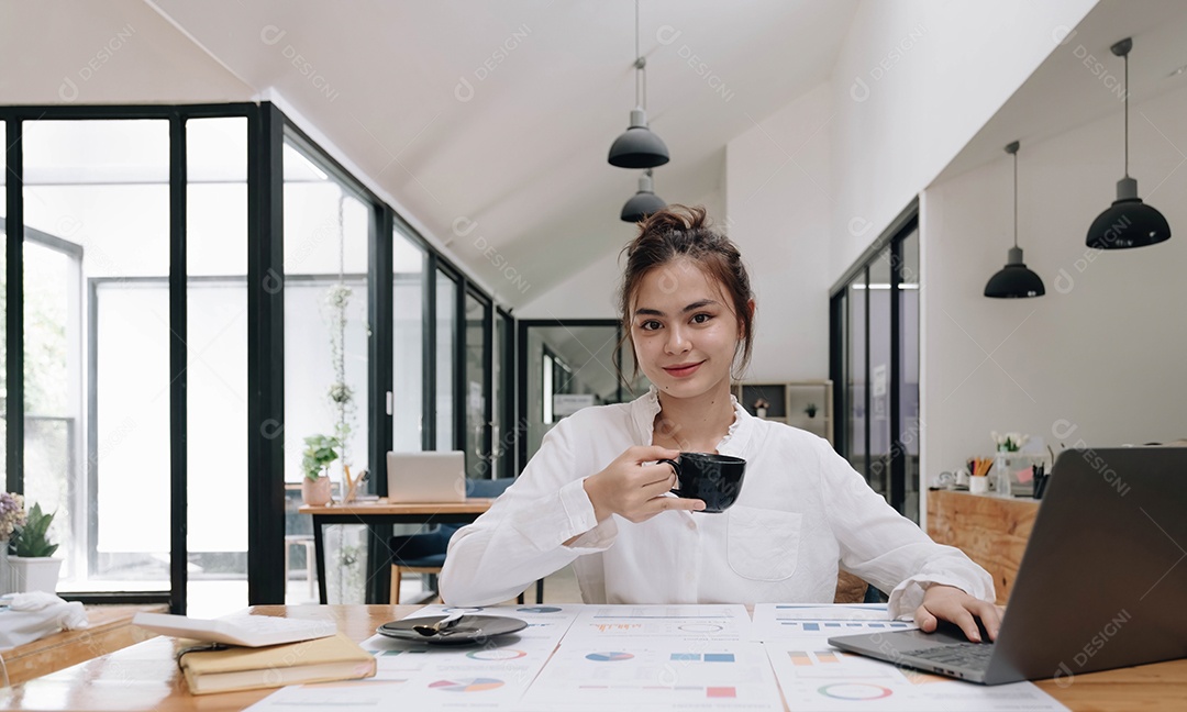 Empresária asiática sorridente segurando uma caneca de café e laptop