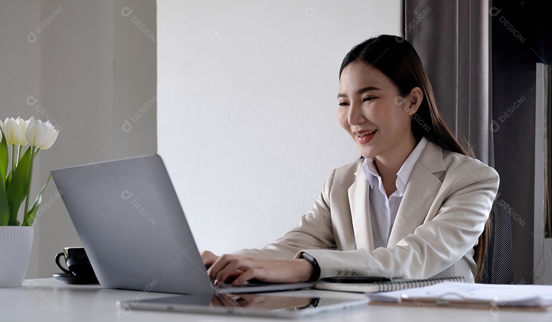 Feliz jovem empresária asiática sentada em seu local de trabalho