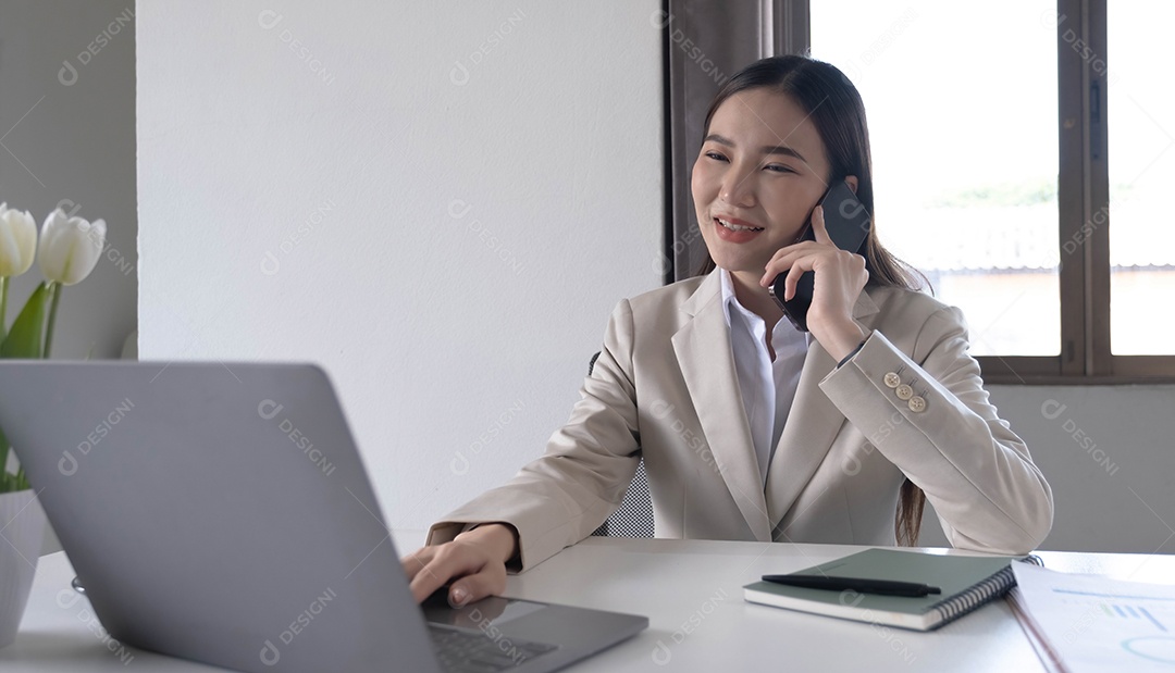 Jovem mulher asiática falando ao telefone usando um laptop