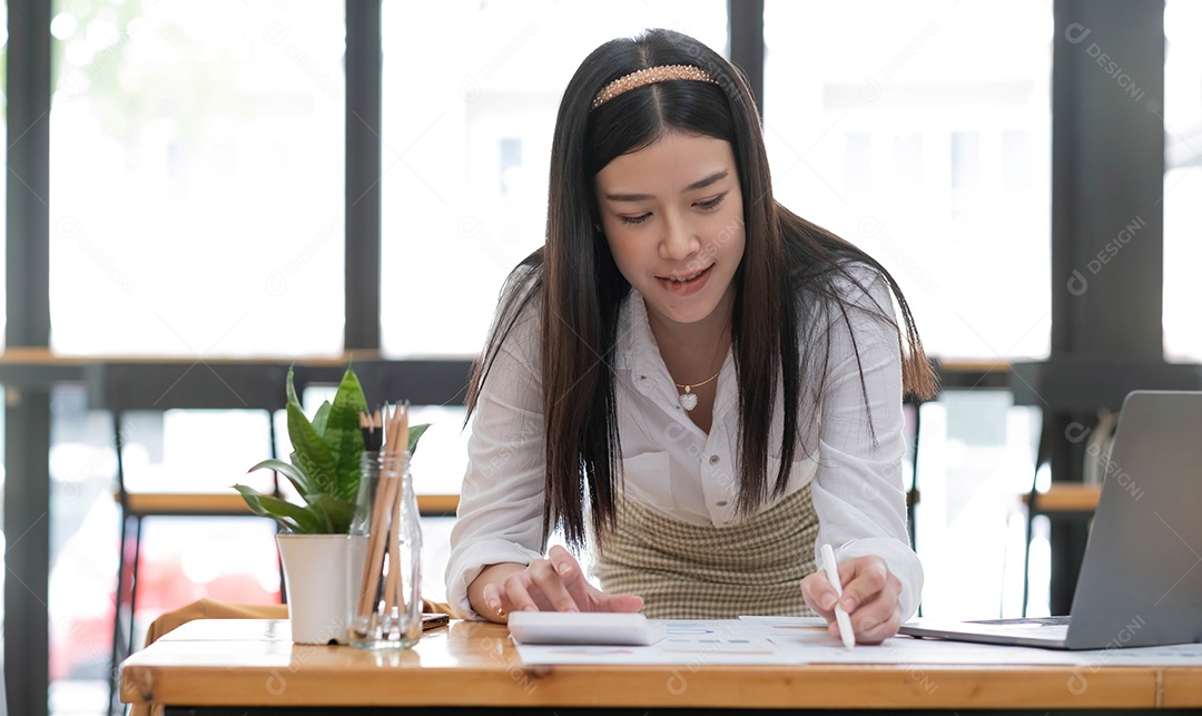 Mulher de negócios que trabalha no escritório de mesa com o uso de uma calculadora