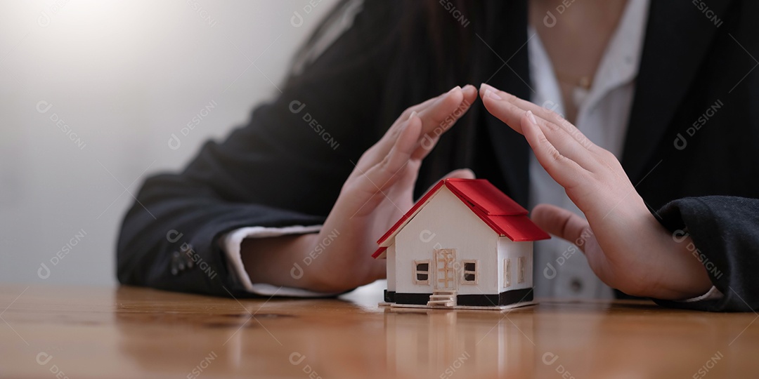 Proteja seu conceito de casa. Casa de brinquedo pequena coberta pelas mãos