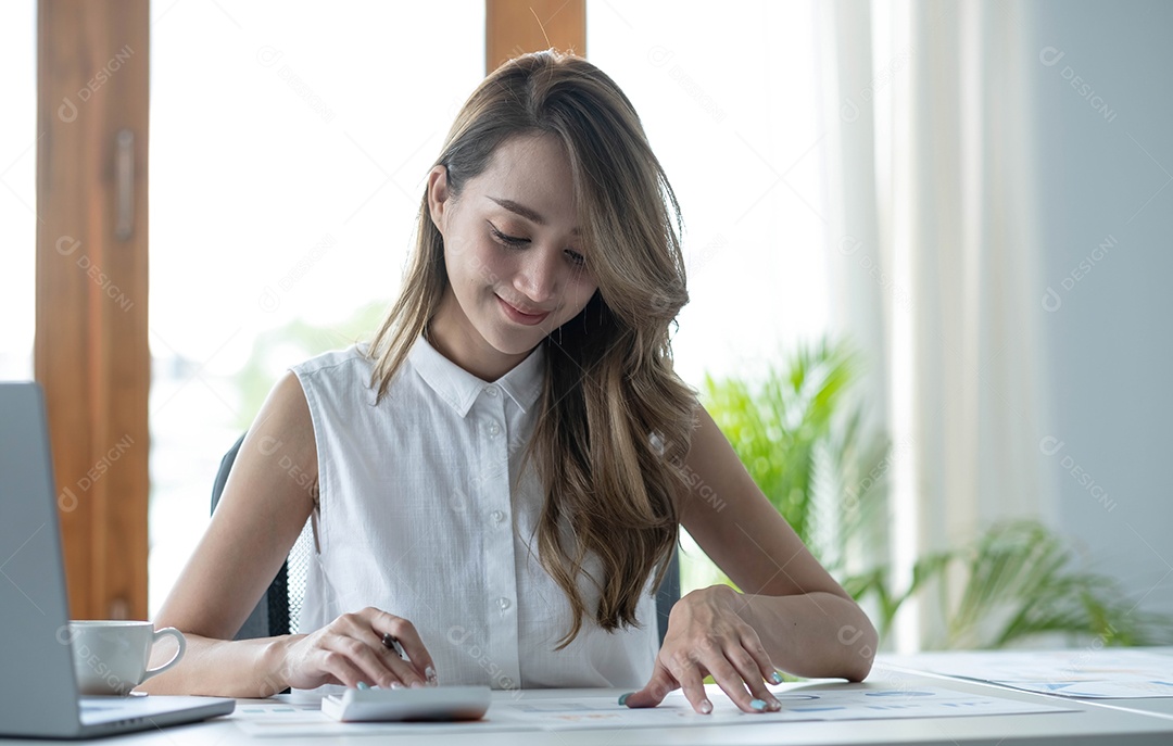Bela empresária asiática analisa gráficos usando calculadora de laptop no escritório.