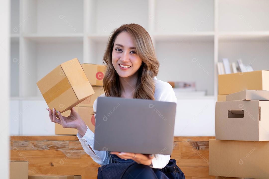 Retrato de uma jovem asiática PME trabalhando com uma caixa em casa