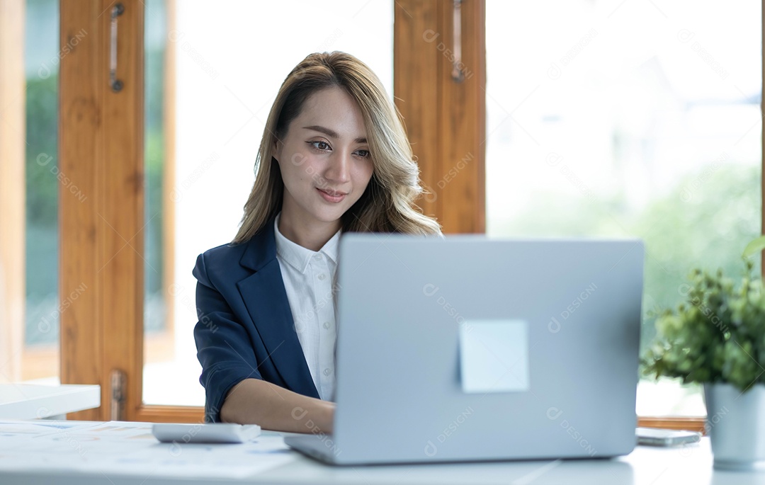 Encantadora empresária asiática sentada trabalhando no laptop no escritório