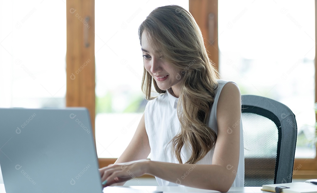 Feliz jovem empresária asiática sentada em seu local de trabalho
