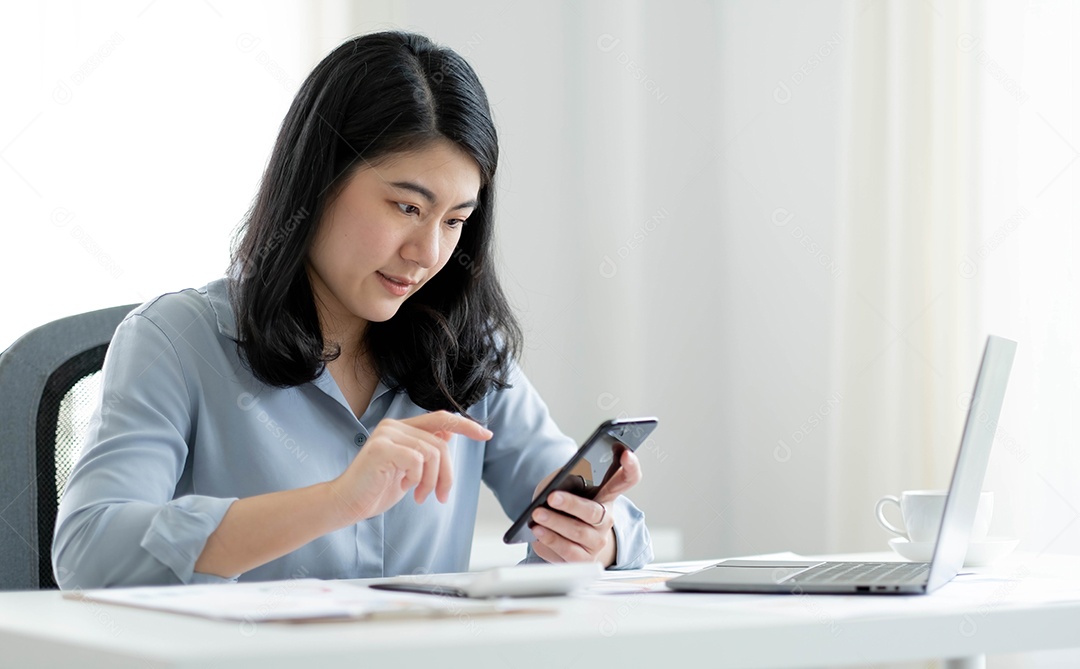 Mulher asiática sentada trabalhando com celular e computador
