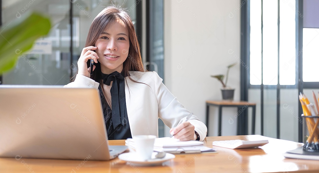 Encantadora empresária asiática trabalhando com um laptop e usando smartphone no escritório.