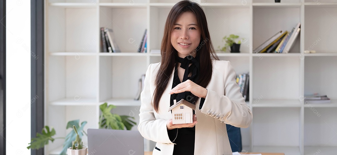 Casa em miniatura nas mãos de uma mulher asiática, corretora de imóveis