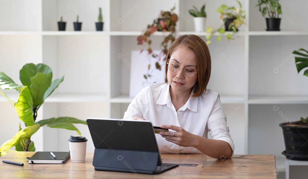 Mulher sênior asiática usando um laptop com cartão de crédito.