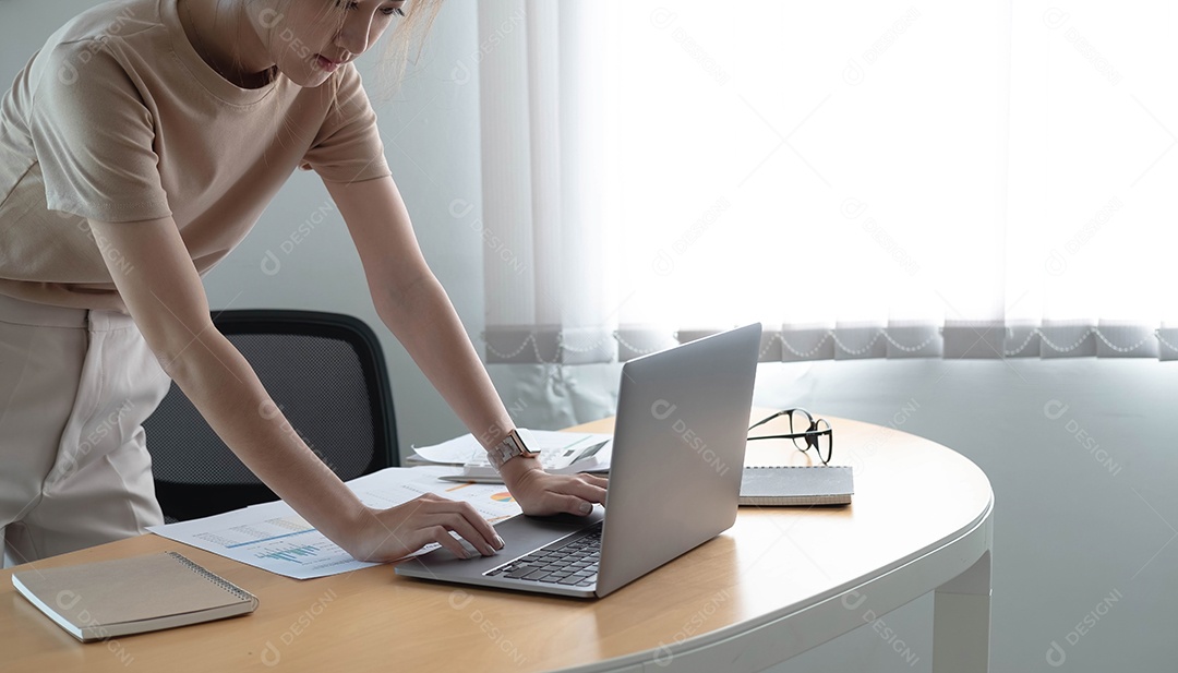 Jovem asiática usando computador portátil em pé em uma sala de escritório.