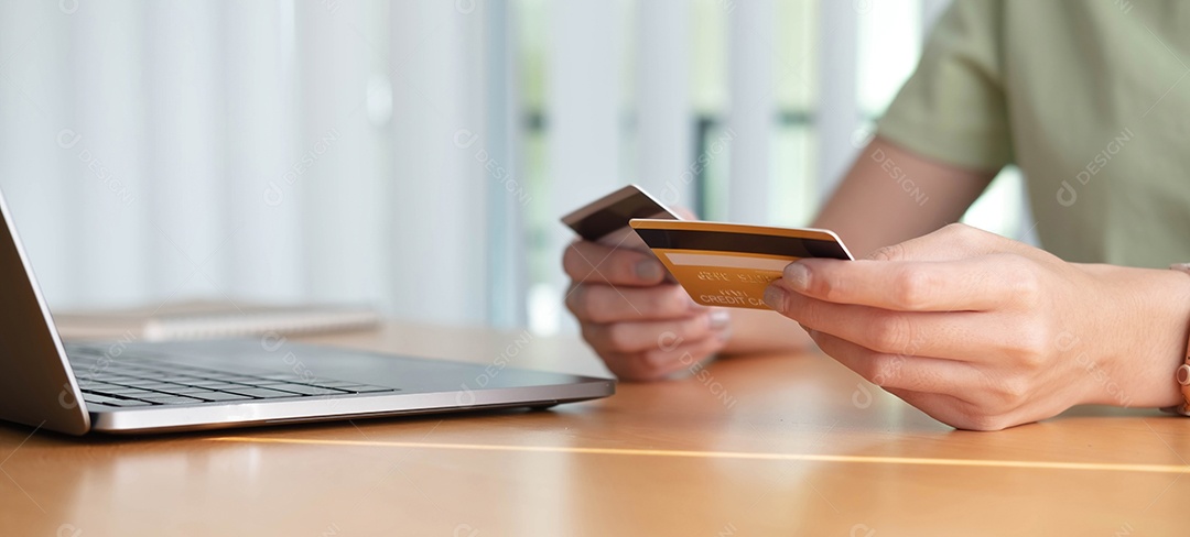 Compras online. Jovem segurando o cartão de crédito e usando o laptop