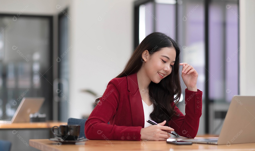 Bela empresária asiática analisa gráficos usando calculadora de laptop no escritório.