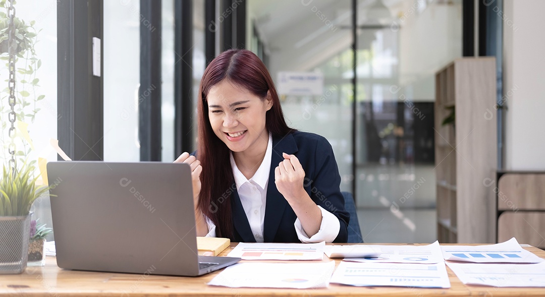 Linda empresária asiática comemora enquanto usa o laptop no escritório e mostra prazer.