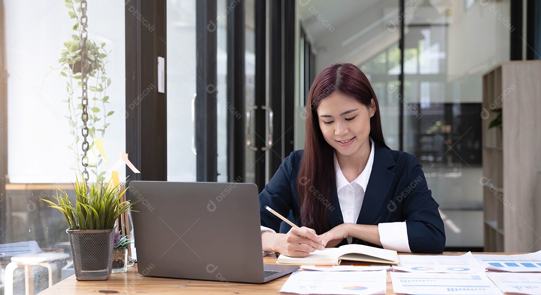 Feliz jovem empresária asiática sentada em seu local de trabalho no escritório.