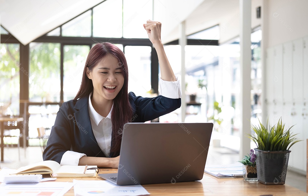 Feliz jovem empresária asiática sentada em seu local de trabalho