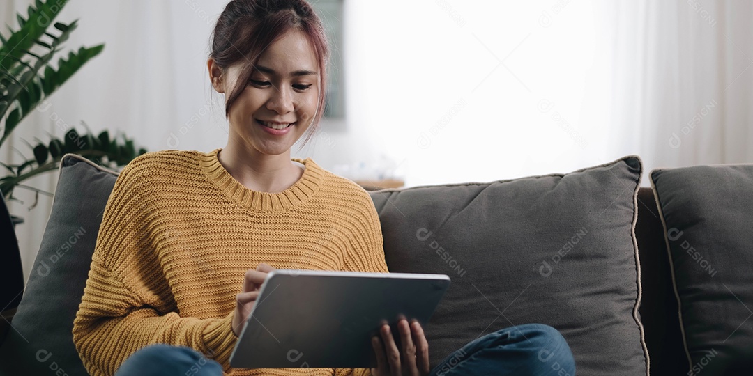 Mulher jovem sorridente usando laptop, sentada no sofá em casa