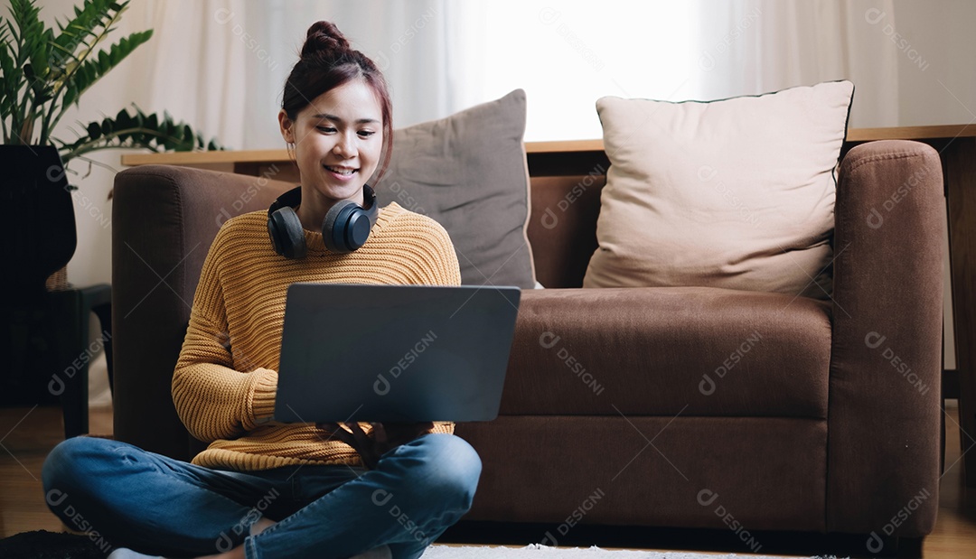 Jovem bonita usando seu laptop enquanto está sentada no chão em casa.