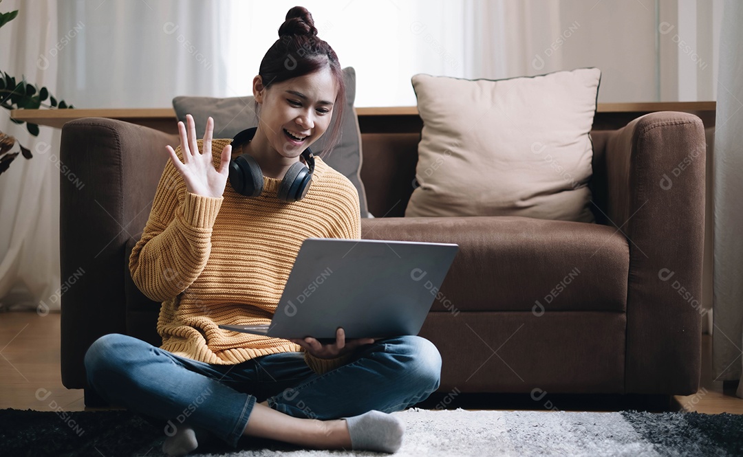 Jovem bonita usando seu laptop enquanto está sentada no chão em casa.